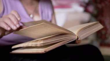 Kitap okuyan yaşlı bir kadın, Kapalı Kapılar 'daki güneş ışınlarında sayfaları çeviriyor. Yakın plan. Bir emeklinin elinde açık bir kitap vardır, çalışır ve emekliliğinde evde dinlenir. Yaşlıların yaşam tarzı..