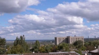 Beyaz tüylü Cumulus Bulutları Eski Şehrin terk edilmiş bir binasının üzerinde Gökyüzü tarafından yüzüyor. Zaman aşımı. Bulut manzarası. Şehrin panoramik manzarası, fabrika ve rüzgarda sallanan ağaçlar. Güneş ışınları, gölge. Çatılar..