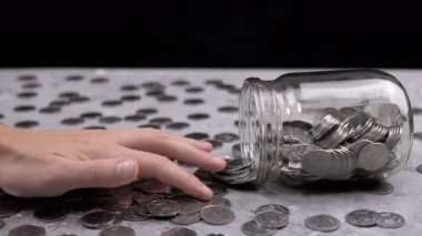 Kadın El, Ters Cam Kavanozdan Masaya Dağılmış Paraları Sayıyor. Gri beton arka planda bir sürü bozuk para var. Finansal kriz, bütçe, tasarruf, para birikimi. Nakit. Yoksulluk.