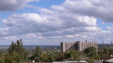 Beyaz tüylü Cumulus Bulutları Eski Şehrin terk edilmiş bir binasının üzerinde Gökyüzü tarafından yüzüyor. Zaman aşımı. Bulut manzarası. Şehrin panoramik manzarası, fabrika ve rüzgarda sallanan ağaçlar. Güneş ışınları, gölge. Çatılar..
