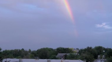 Eski şehrin çatısının üstündeki kasvetli gökyüzünde çok renkli parlak gökkuşağı. Şehrin uzun yeşil ağaçlı panoramik manzarası. Yağmurdan sonra gökkuşağı. Ufuk çizgisinde güzel bir doğa olayı.