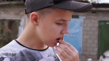 Garajın yakınında aç çocuk cips ya da kraker yiyor. Şapkalı ve tişörtlü bir çocuğun portresi. Yan görüş. Sağlıksız fast food yiyorum. Açık havada. Dinleniyor. Çocuk yaşam tarzı.