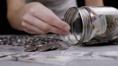 Cam kavanozu gümüş para ve 100 dolarlık banknotlarla dolduran kadın. Domuz kumbarası. Beton zeminde Ukrayna sentleri ve nakit para yatıyor. Bütçe, ödeme, harcamalar, tasarruflar. Finansal kriz. Stok.