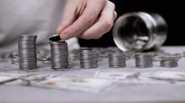 Hands Building a Coin Tower or Stack against the Background of Scattered Money. Piggy bank. Hand places one silver cent on top of a tower in descending order of height. Budget, spending, savings.