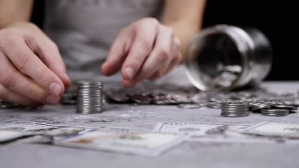 女性的手从散落的钱旁边的一堆堆硬币中建造一座塔 玻璃瓶 猪银行 手把银币放在塔顶上 — 图库视频影像