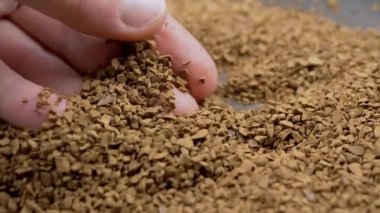 Female Hand Touches with Fingers the Granules of Loose Instant Coffee in Pile. Close up. Hands are holding, sorting through brown particles of coffee beans on a coffee background. Texture, light.