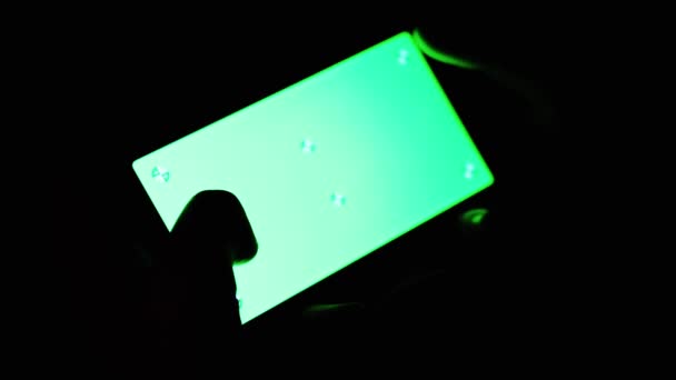 黑色房间里 男性手拿着绿色屏风色钥匙的手机 靠近点用手指触摸智能手机屏幕的人 在晚上看带有绿色笑料的电话录像 — 图库视频影像