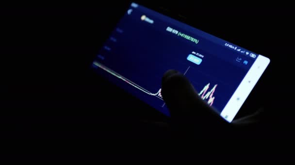 暗い部屋で夜の携帯電話アプリで暗号通貨チャートを表示する男性 トレーダーは指でスマートフォンの画面に触れます 動力学統計成長秋 証券取引所 将来の価格 ビットコイン — ストック動画