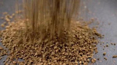 Instant Coffee Granules Fall and Scatter into a Heap on a Black Background. Slow motion. Close up. A stream of brown powder, gold particles, soluble coffee granules flies into a pile. Texture, light.