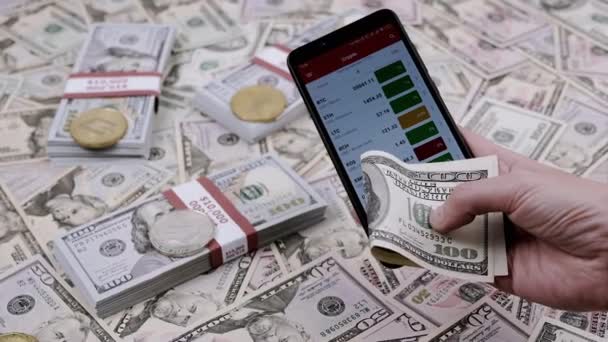 男子手持100美元钞票和手机 背景模糊 交易员在智能手机屏幕上分析应用程序中加密货币的价格 加密货币投资 — 图库视频影像