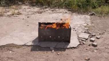 Açık havada dumanlı odun sobasında parlak bir alevle doğranmış odun yanığı. Güneş ışığının altında beton asfalt üzerinde duran bir ızgarada yanan kırmızı bir şenlik ateşi. Arka bahçe.