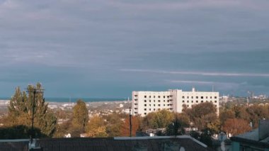 Terk Edilmiş Bir Binanın Arkaplanında Gri Kümülüs Bulutları Taşımak. Eski şehrin kasvetli manzarası. Fabrika. Gölge. Çatı katları. Ağaçlar sallanıyor. Rüzgâr. Bulutlu. Ufuk. Gün batımı. Parlak güneş ışınları.