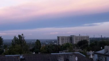 Pembe Gri Günbatımı Endüstri Şehri üzerinde. Zaman ayarlı. Eski evlerin çatılarında yavaşça bulutların hareketi. Romantik bulutlu manzara. Fabrika. Ağaçlar sallanıyor. Rüzgâr. Bulutlu. Ufuk. Şehir manzarası.