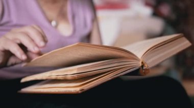 Kitap okuyan yaşlı bir kadın, Kapalı Kapılar 'daki güneş ışınlarında sayfaları çeviriyor. Yakın plan. Emeklinin biri elinde bir kitap tutuyor, okuyor ve emekliliğinde evde dinleniyor. Yaşlıların yaşam tarzı..