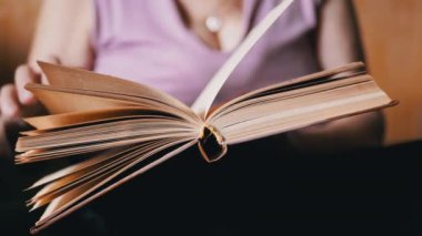 Kitap okuyan yaşlı bir kadın, Kapalı Kapılar 'daki güneş ışınlarında sayfaları çeviriyor. Yakın plan. Bir emeklinin elinde açık bir kitap vardır, çalışır ve emekliliğinde evde dinlenir. Yaşlıların yaşam tarzı..