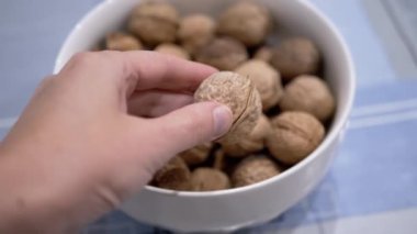Çiftçi Eller Masadaki Ceviz Kasesinden Bir Fındık Aldı ve Tuttu. Yakın plan. Sonbahar hasadı olgun, taze ceviz. Faydalı sağlıklı yiyecekler. Beyin gıdası. Diyet yemek. Vejetaryenlik. Ceviz kabuğu.