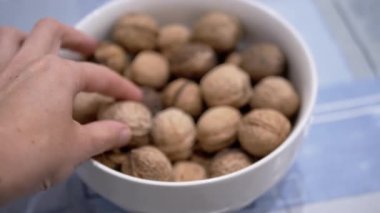 Çiftçi Eller Masadaki Ceviz Kasesinden Bir Fındık Aldı ve Tuttu. Yakın plan. Sonbahar hasadı olgun, taze ceviz. Faydalı sağlıklı yiyecekler. Beyin gıdası. Diyet yemek. Vejetaryenlik. Ceviz kabuğu.