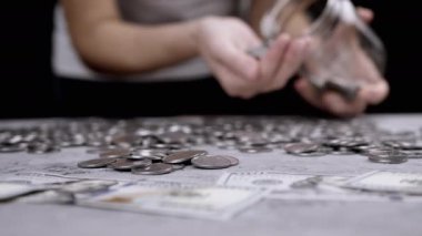 Kadın, Cam Kavanoz 'dan Birikmiş Gümüş Para Yığını Bir Masaya Döker. Gri beton arka planda bir sürü bozuk para var. Finansal kriz, bütçe, tasarruf, para birikimi. Sayıyorum. Yoksulluk.