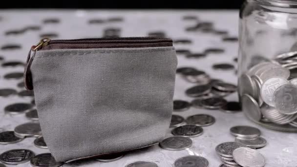 女人把一些钱放进一个零钱灰色钱包里 散落的乌克兰银币 玻璃储蓄罐躺在一张桌子模糊的背景上 — 图库视频影像