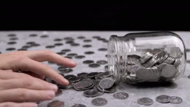 Kadın El, Ters Cam Kavanozdan Masaya Dağılmış Paraları Sayıyor. Gri beton arka planda bir sürü bozuk para var. Finansal kriz, bütçe, tasarruf, para birikimi. Nakit. Yoksulluk.