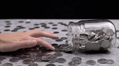 Kadın El, Ters Cam Kavanozdan Masaya Dağılmış Paraları Sayıyor. Gri beton arka planda bir sürü bozuk para var. Finansal kriz, bütçe, tasarruf, para birikimi. Nakit. Yoksulluk.