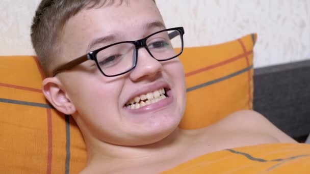 Adolescent Ochelari Întinși Pat Face Fețe Arată Dinți Grimacing Băiat — Videoclip de stoc