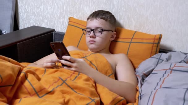 Adolescente Óculos Escrevendo Mensagens Texto Smartphone Deitado Uma Cama Acolhedora — Vídeo de Stock