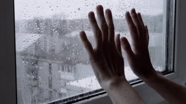 Kadın Islak Pencere 'ye İki Elle Dokunur. Parmaklar ıslak bardakta kayıyor. Yoğuşma akışının damlaları aşağı akıyor. İzolasyon evde. Kasvetli yağmurlu bir gün. Umut, ayrılık, umutsuzluk, özlem, yalnızlık.