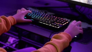 Hands Gamer sanal gerçeklik kulübündeki bir video oyununda RGB klavyesini çalıyor. Yakın plan. Hacker parmaklarıyla düğmelere basıyor, fareyi halının üzerinde hareket ettiriyor. Neon ışıkları. Kumar oynuyorum. ESports. VR.