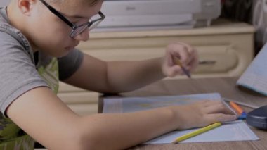 Gözlüklü Ciddi Çocuk Dünya Haritasına Kalemle Vuruşlar Çiziyor. Üzgün bir okul çocuğu masada oturuyor, coğrafya ödevi yapıyor. Kırtasiye malzemeleri. Eğitim konsepti. İç mekan. Büyüt.