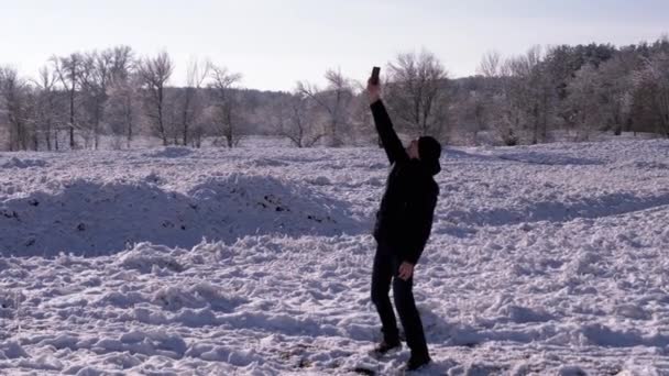 在冬季雪地的森林里 年轻的雄性试图捕捉一个信号 一个快乐的家伙在雪地上跳着 手伸向蓝天 寻找一个连接 没有信号 威菲生活方式 — 图库视频影像