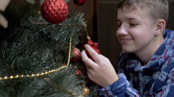 笑顔の男の子は クリスマスツリー上の素敵な光沢のあるぶら下がりクリスマスツリーおもちゃを調べます パジャマ姿の幸せな子供は 輝く赤いボールのおもちゃでクリスマスツリーを飾ります クリスマスの飾り 幸せな家族だ — ストック動画