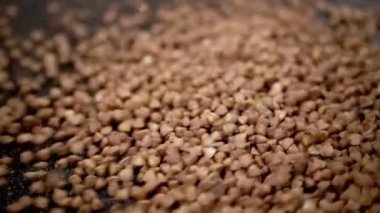 Grains of Buckwheat Fall on a Black Background in Slow Motion. Close up. Raw brown granules and buckwheat particles pour into a pile of buckwheat. Falling buckwheat fills a grainy surface. Texture.