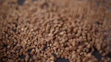 Grains of Buckwheat Fall on a Black Background in Slow Motion. Close up. Raw brown granules and buckwheat particles pour into a pile of buckwheat. Falling buckwheat fills a grainy surface. Texture.