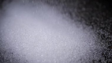 Granulated Sugar 'ın Beyaz Kristalleri Yavaş Çekimde Siyah Arkaplan' a Düşüyor. Yakın plan. Şeker parçacıkları akışı yüzeyi doldurur. Granüller. Doku, soyut arkaplan. Şeker tüketimi.