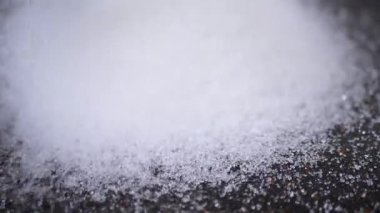 Granulated Sugar 'ın Beyaz Kristalleri Yavaş Çekimde Siyah Arkaplan' a Düşüyor. Yakın plan. Şeker parçacıkları akışı yüzeyi doldurur. Granüller. Doku, soyut arkaplan. Şeker tüketimi.