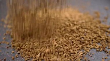 Instant Coffee Granules Fall and Scatter into a Heap on a Black Background. Slow motion. Close up. A stream of brown powder, gold particles, soluble coffee granules flies into a pile. Texture, light.