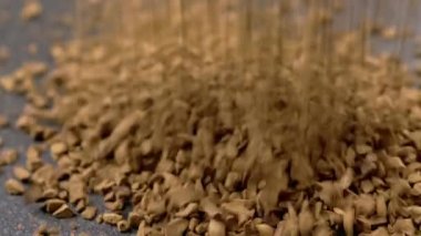 Instant Coffee Granules Fall and Scatter into a Heap on a Black Background. Slow motion. Close up. A stream of brown powder, gold particles, soluble coffee granules flies into a pile. Texture, light.
