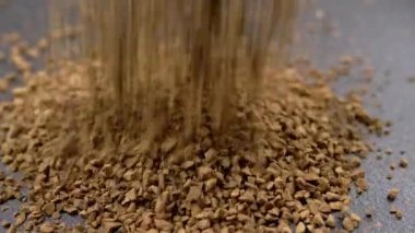 Instant Coffee Granules Fall and Scatter into a Heap on a Black Background. Slow motion. Close up. A stream of brown powder, gold particles, soluble coffee granules flies into a pile. Texture, light.