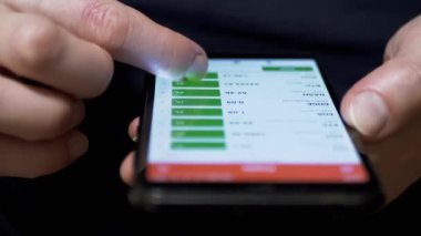 Yatırımcı, bir cep telefonunun dokunmatik ekranında kripto para biriminin fiyatını kontrol ediyor. Parmaklar akıllı telefonun ekranına değiyor. Mobil uygulama. Kripto para çiftleri, bitcoin. Borsa verileri. Büyüme, kriptonun düşüşü.