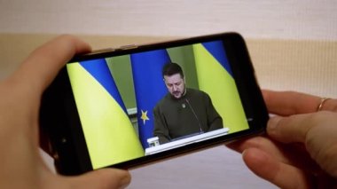 UKRAINE, KAMENSKOE, FEBRUARY, 2023: Bir Cep Telefonu Ekranında Ukrayna Başkanının Konuşmasını İzleyen Kadın. Dünya haberleri. Vladimir Zelensky 'nin Ukrayna halkına akıllı telefondan seslenişi.