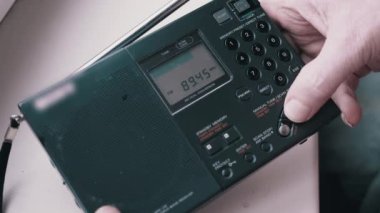 Kara Tozlu Modern Taşınabilir Radyo Alıcısı 'nda Frekans Bulmak. Erkek parmakları düğmeye basarak FM dalgalarını arayın. İkili dönüşüm, elle akort, tarama istasyonu. Dijital ekran, kanal değişimi.