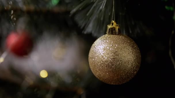金新圣诞舞会挂在灯火背景下的云杉树枝上 靠近点圣诞树装饰易碎球 模糊的背景和闪烁的Led灯 圣诞装饰 — 图库视频影像