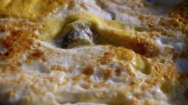 Yakın plan pişirme, çırpılmış yumurta kızartma tavasında güneş ışığı altında. Kahverengi omlet kabuğu dokusu, kabartma, yüzey, arka plan. Sarısı. Yakın plan çıtır çıtır. Kamera hareketi. - Günaydın. Gün doğumu.