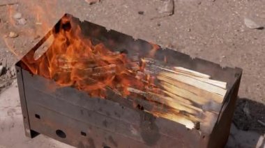Açık havada dumanlı odun sobasında parlak bir alevle doğranmış odun yanığı. Kızgın kırmızı bir şenlik ateşi, beton asfalt ve güneşin altında duran bir ızgara ızgarasında. Hafta Sonu.