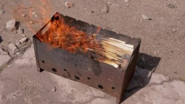 Açık havada dumanlı odun sobasında parlak bir alevle doğranmış odun yanığı. Kızgın kırmızı bir şenlik ateşi, beton asfalt ve güneşin altında duran bir ızgara ızgarasında. Hafta Sonu.