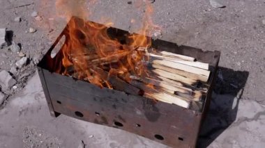 Açık havada dumanlı odun sobasında parlak bir alevle doğranmış odun yanığı. Kızgın kırmızı bir şenlik ateşi, durgun bir ızgarada, güneş ışığının arka bahçesinde beton asfalt üzerinde duruyor..