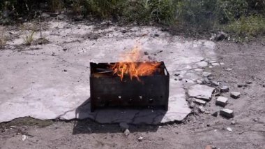 Açık havada dumanlı odun sobasında parlak bir alevle doğranmış odun yanığı. Kızgın kırmızı bir şenlik ateşi, durgun bir ızgarada, güneş ışığının arka bahçesinde beton asfalt üzerinde duruyor..