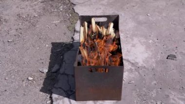 Açık havada dumanlı odun sobasında parlak bir alevle doğranmış odun yanığı. Kızgın kırmızı bir şenlik ateşi, durgun bir ızgarada, güneş ışığının arka bahçesinde beton asfalt üzerinde duruyor..