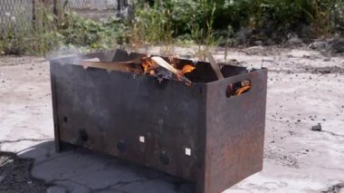 Açık havada dumanlı odun sobasında parlak bir alevle doğranmış odun yanığı. Kızgın kırmızı bir şenlik ateşi, durgun bir ızgarada, güneş ışığının arka bahçesinde beton asfalt üzerinde duruyor..